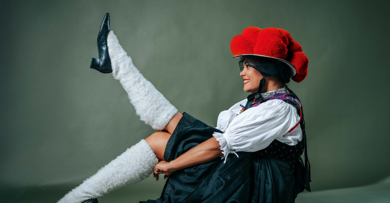 Junge Frau in traditioneller Schwarzwälder Bollenhut-Tracht posiert mit Bein in die Luft und augenzwinkerndem Lächeln