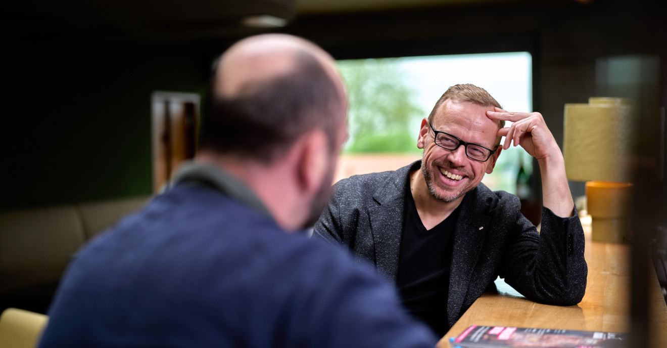 Ulf Tietge im Interviewgespräch an einem Tresen, lachend im Gespräch mit einem Gegenüber